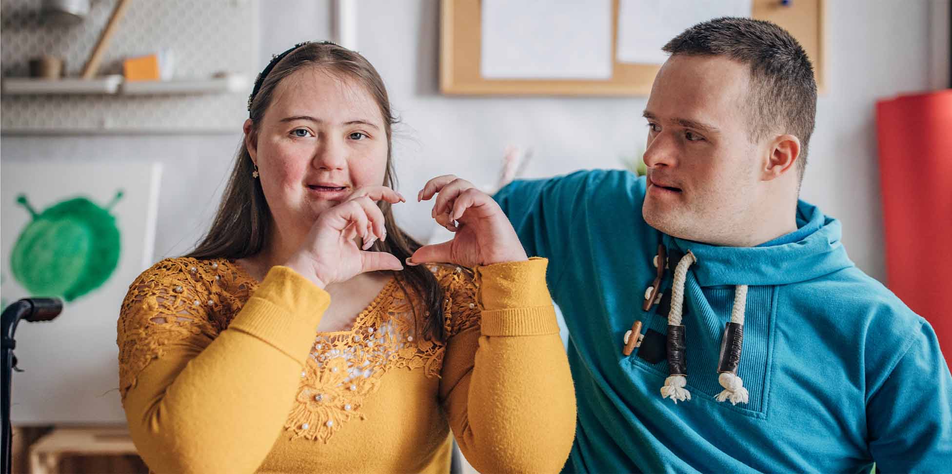 konzept_entwicklung Mädchen zeigt Herz in die Kamera, Junge sitzt daneben und schaut sie an