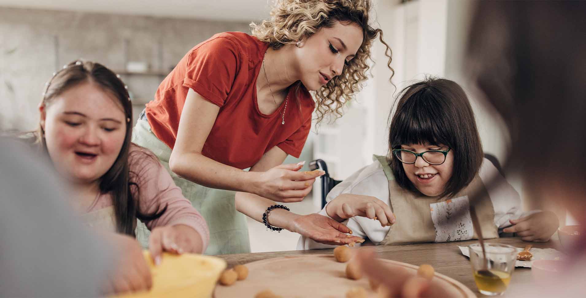konzept_fuerwen Zwei Behinderte Mädchen backen gemeinsam mit einer Betreuerin
