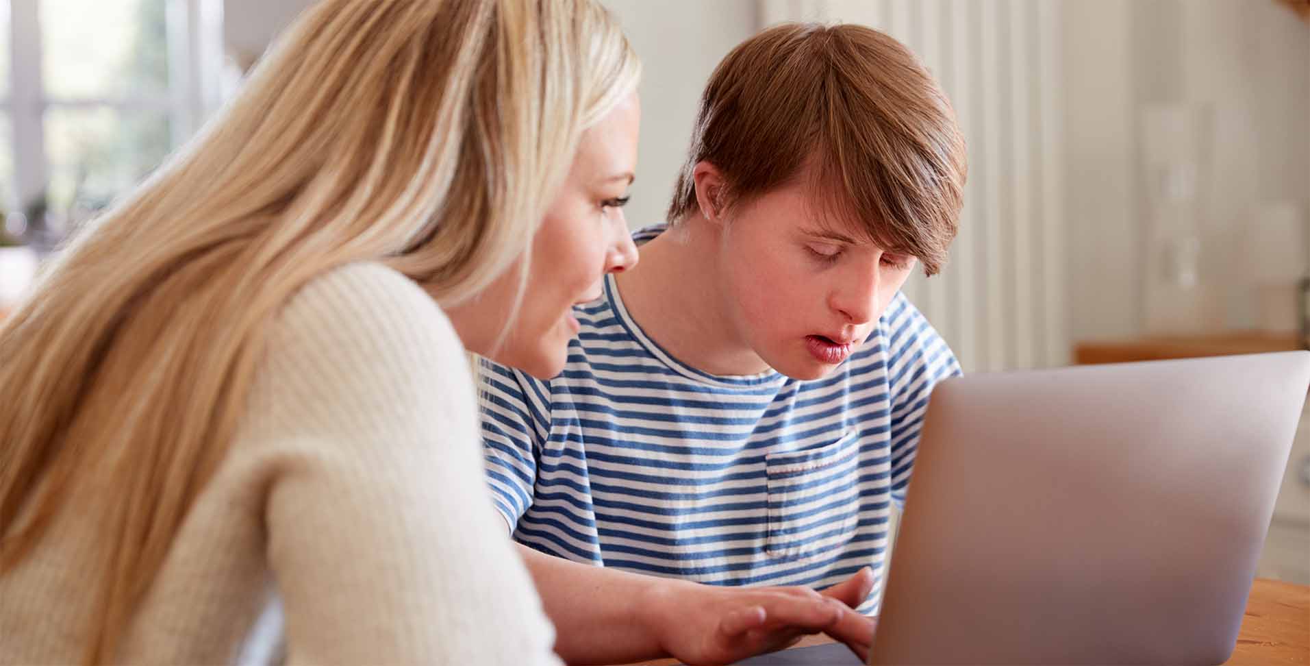 konzept_tagesablauf Betreuerin unterstützt behinderten Jungen am Laptop